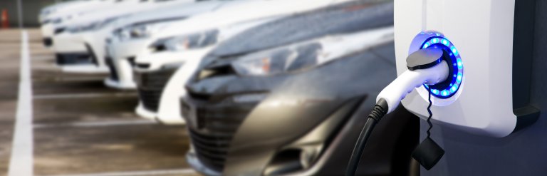 Photograph of in-use car charging point in the foreground with out of focus cars in the background